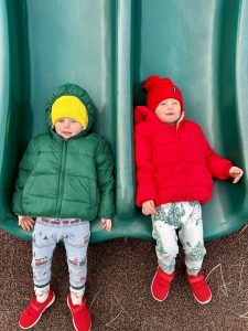 two boys under 3 years old on the bottom of a slide with red and green jackets