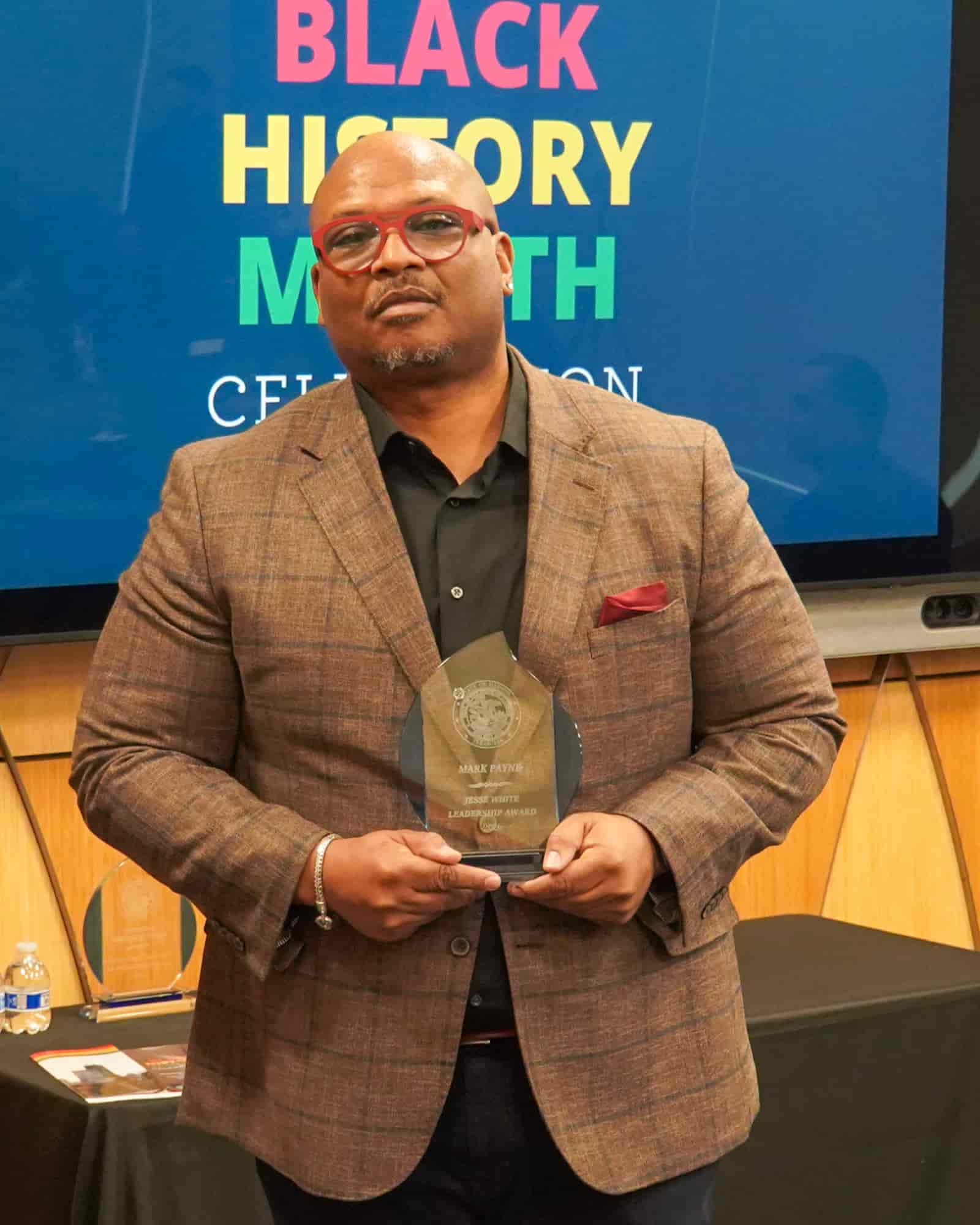 man wearing glasses and a suit holding an award with pride