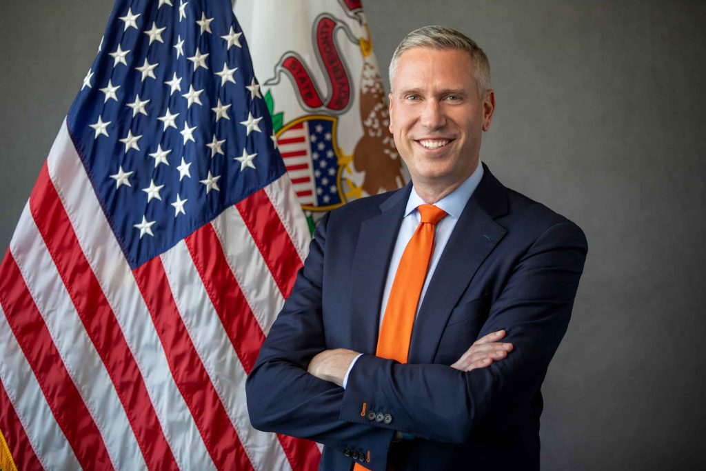 treasurer with arms crossed in front of american and illinois flags