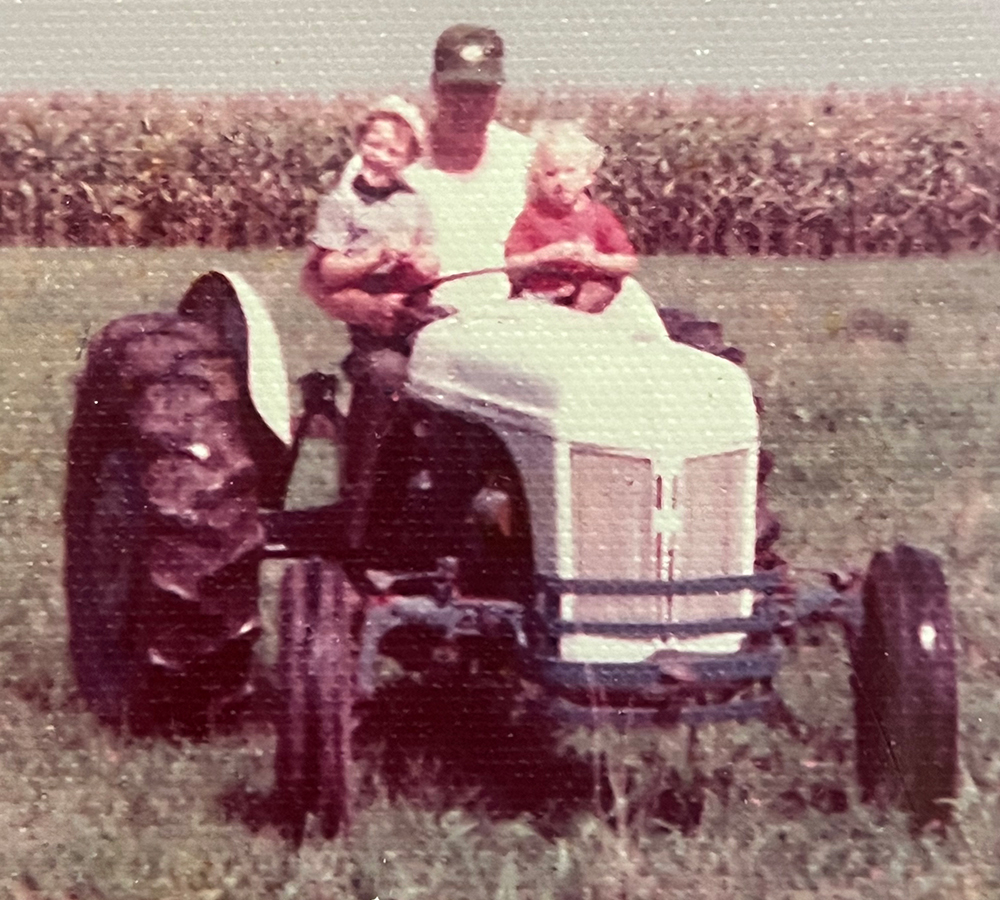 A man wearing a cap as he sits on a tractor and holds two toddler boys on his lap