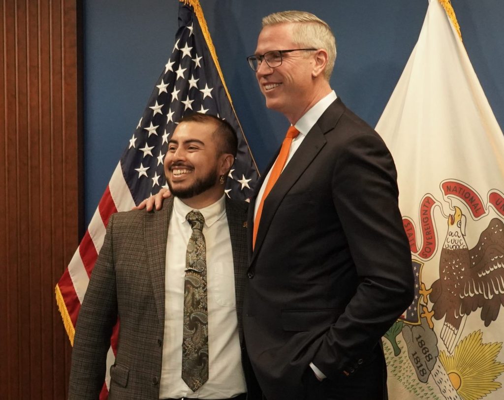 two men in suits standing in front of the illinois flag and united states flag